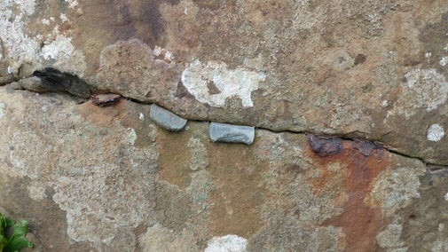 A crack across the rock at the Giant's Causeway has coins, some bent have been hammered into it, some are corroding leaving red rust stains.